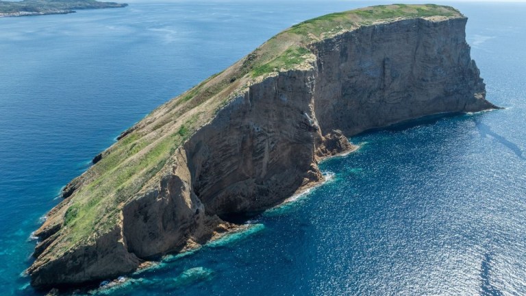 Aerial view of a steep, rocky island surrounded by blue ocean water.
