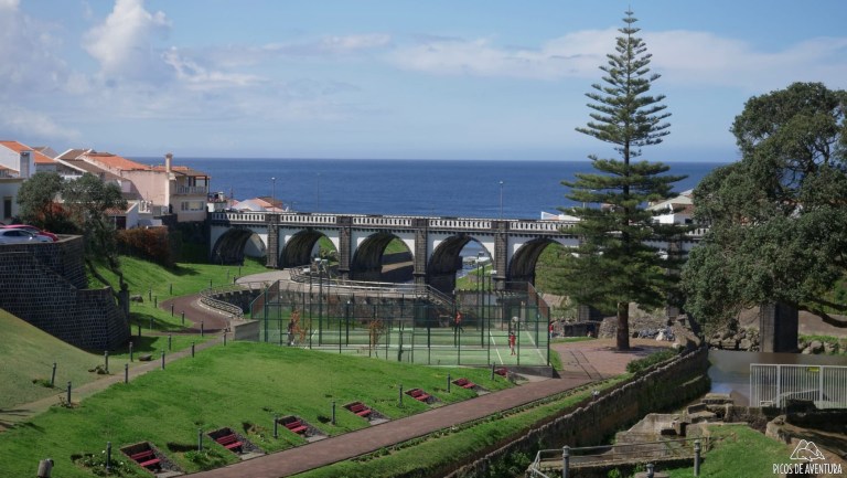 Scenic view of arch bridge, park, and ocean in background on a sunny day.