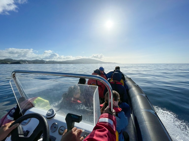 People on a speedboat with distant mountains under a sunny sky.