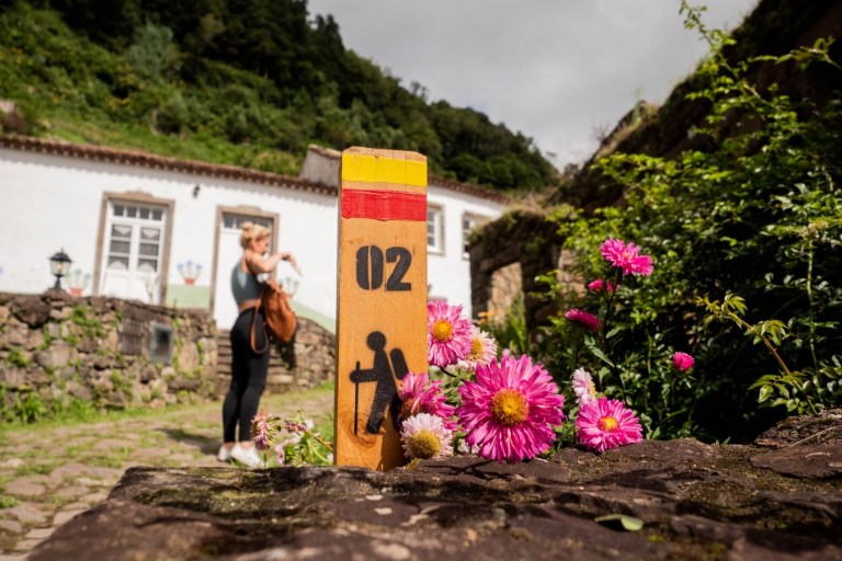 Trail marker with flowers and person in village setting.