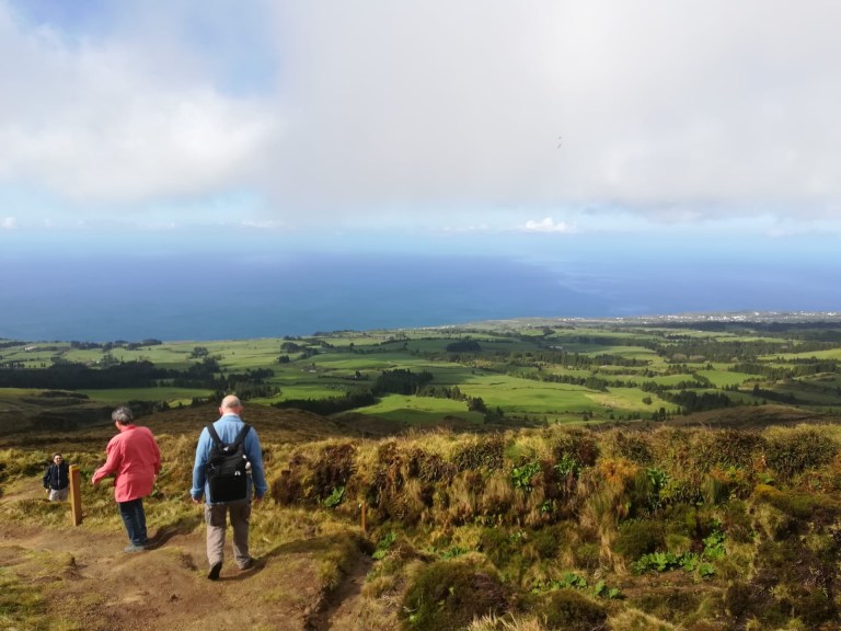 People walking down a grassy hill overlooking a wide landscape and ocean.