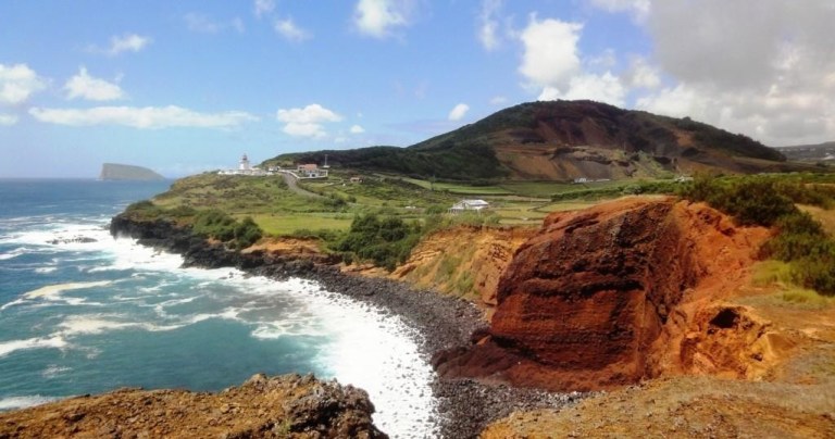 Coastal landscape with cliffs, lighthouse, and ocean under a partly cloudy sky.