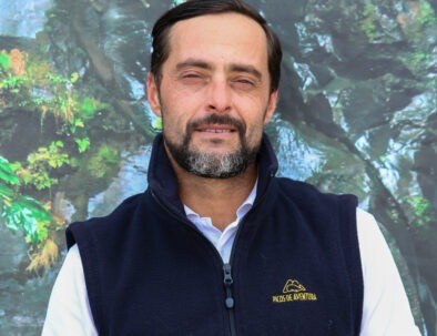 Man wearing a navy vest stands in front of a forest background.