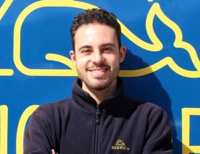 Person smiling in front of a blue and yellow sign with a whale design.