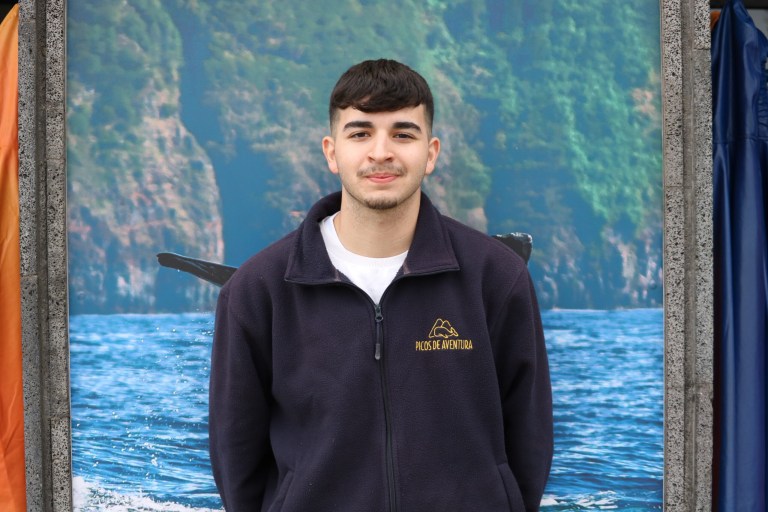 Person in jacket standing with ocean and cliffs background.