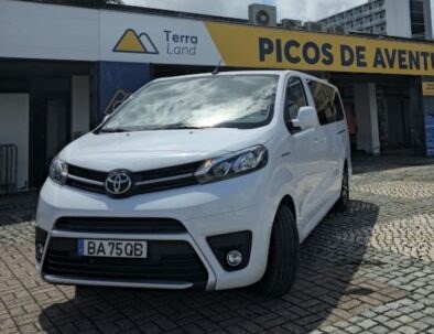 White Toyota van parked on cobblestone near Picos de Aventura sign.