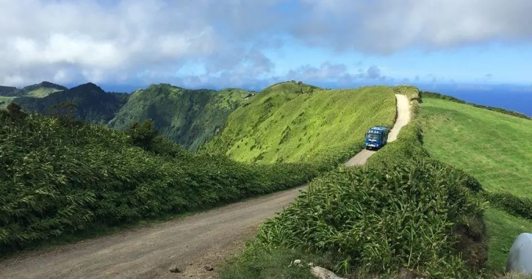 Blue van on a dirt road winding through green hills under a cloudy sky.