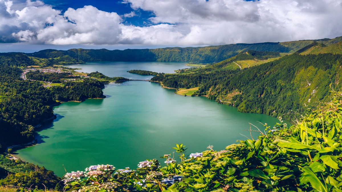 Scenic view of a lake surrounded by green hills under a cloudy sky.
