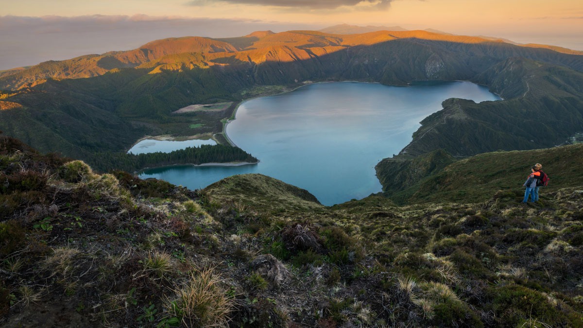 Lush mountain landscape with two lakes at sunset, person standing on hillside.
