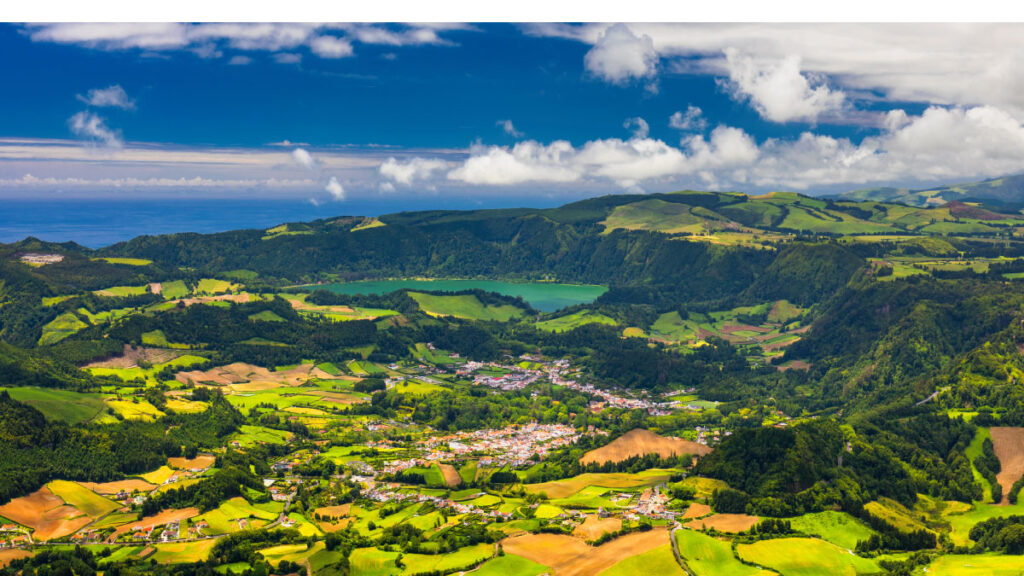 Aerial view of vibrant green fields and a distant lake under a partly cloudy sky.