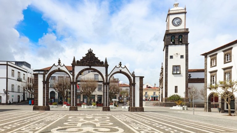 White building with arches and clock tower in a plaza.