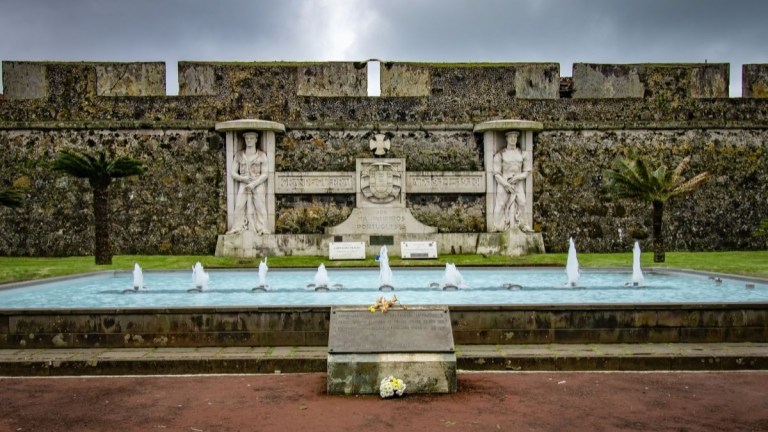 Ornate stone wall with fountain and statues in front of cloudy sky