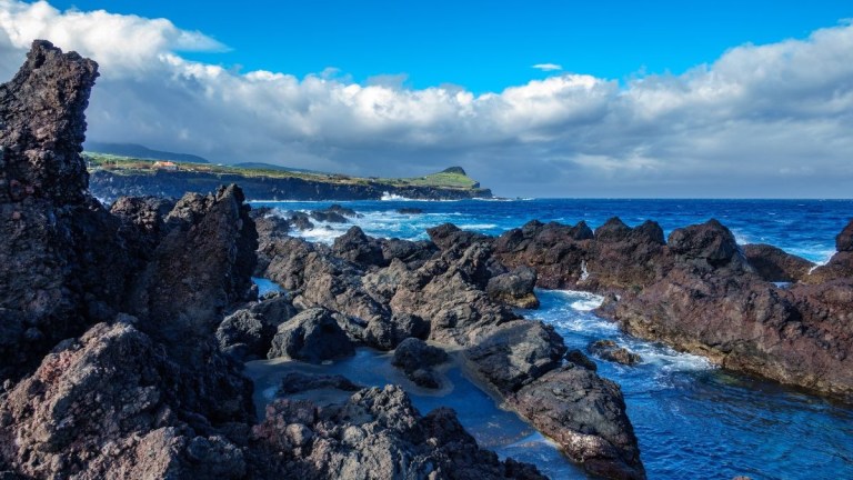 Rocky coastline with blue ocean and cloudy sky.