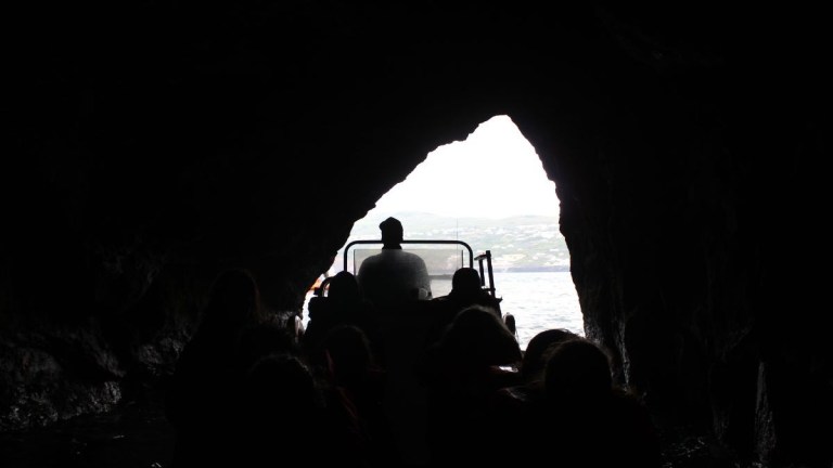 Silhouette of people in a boat exiting a rocky cave.