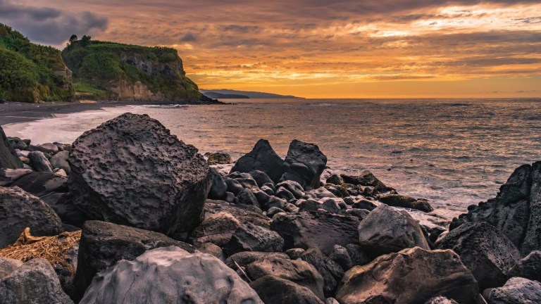 Rocky beach with cliffs at sunset and cloudy sky in the background.