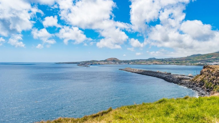 Coastal landscape with blue sea, green hills, and cloudy sky.