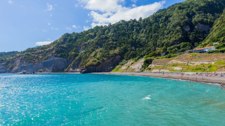 Scenic view of turquoise sea with rocky coastline and green hills under a blue sky.