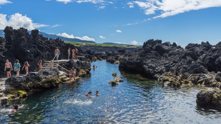 People swimming in a natural rocky pool with blue sky above.