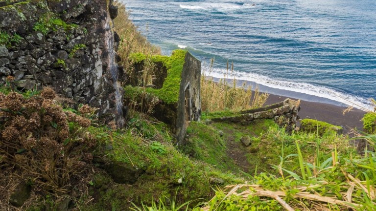 Stone path leads down to a black sand beach by a rocky coastline.