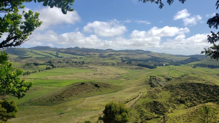 Lush green hilly landscape under a cloudy blue sky.