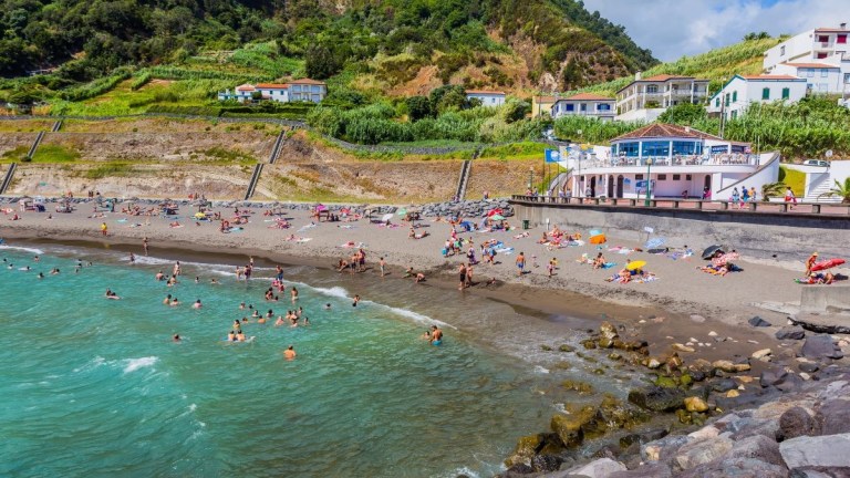 People enjoying a beach with green hills and buildings in the background.