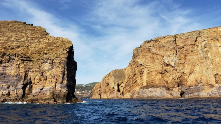 Rocky cliffs above a blue ocean under a partly cloudy sky.