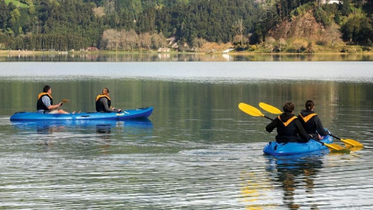 Four people kayaking on a calm lake under a cloudy sky.