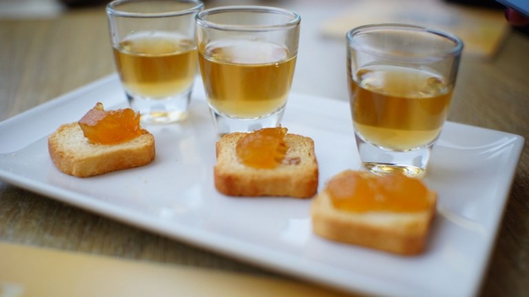 Three shots of amber liquid and toast with orange jelly on a white plate.