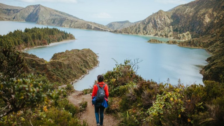 Person in red jacket hiking towards a scenic lake in a mountainous area.