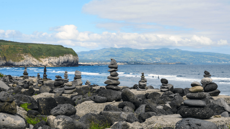 Stone cairns on a rocky beach with cliffs and ocean view.
