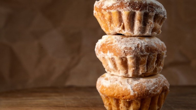 Three stacked, powdered muffins on a wooden surface.