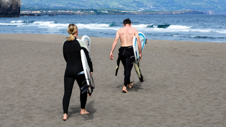 Two surfers walking on beach carrying surfboards towards ocean.