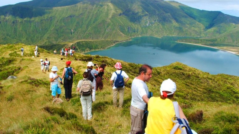 People hiking on a grassy hill overlooking a lake and mountains.