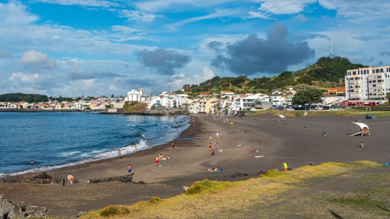 Sandy beach with people, town in the background, and partly cloudy sky.