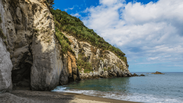 Rocky coastal cliffs beside a calm sea under a partly cloudy sky.