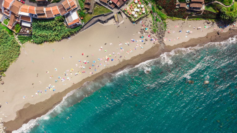 Aerial view of a beach with colorful umbrellas, people, and waves hitting the shore.