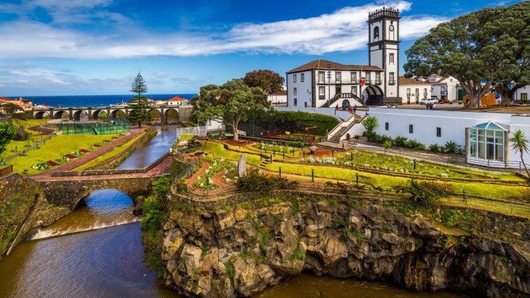 Scenic view of a church and garden by a river with a stone bridge.