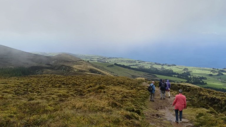 People hiking along a grassy hillside path under a cloudy sky.