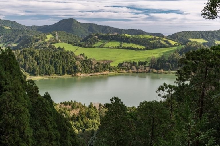 Scenic view of a lake surrounded by lush green hills and forests under a cloudy sky.