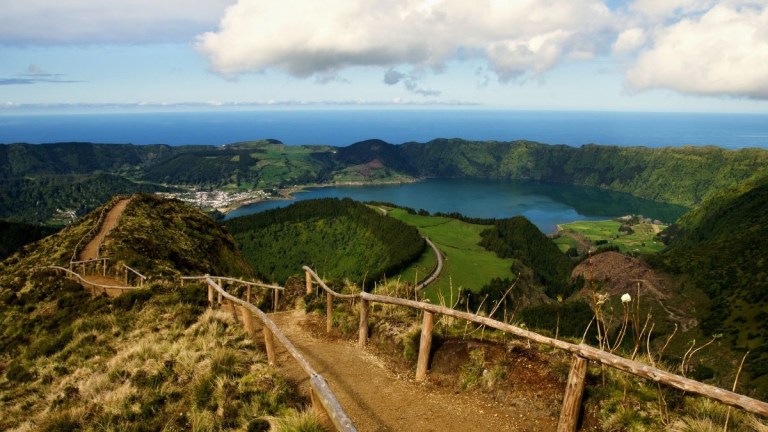 Scenic view of a hilly landscape, lake, and ocean under a cloudy sky.