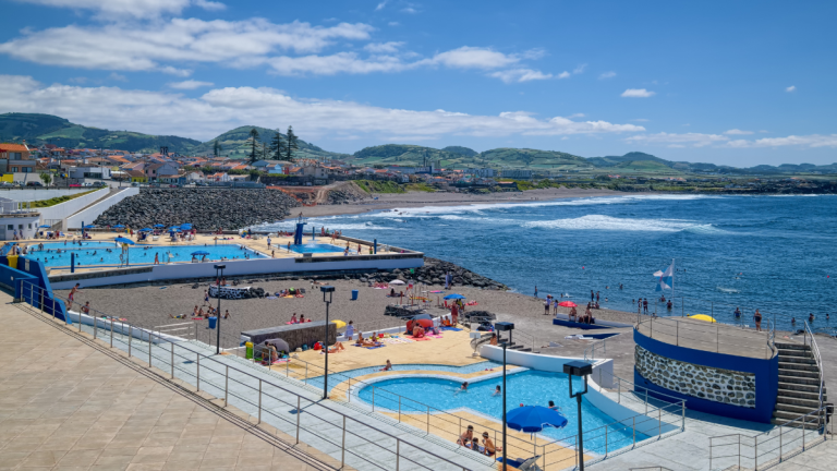 Coastal pool area with ocean view, lounge chairs, and people swimming.