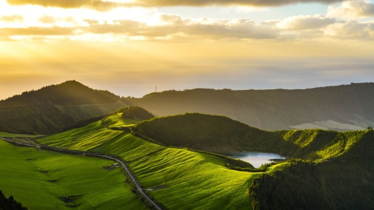Sunset over rolling green hills and a small lake with golden clouds in the sky.