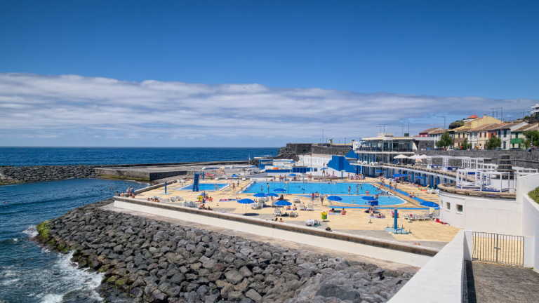Coastal pool area with umbrellas, blue sky, and ocean view.