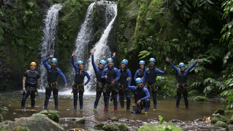 Group of people in helmets and wetsuits posing by a waterfall.