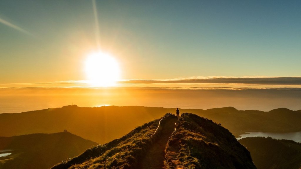 Person standing on a hill at sunrise with a clear sky.