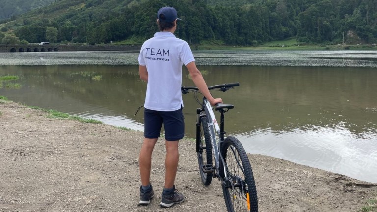 Person in sportswear with a bike, facing a lake and hills in the background.