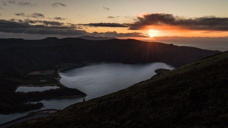 Sunset over a valley with a large lake and surrounding hills.