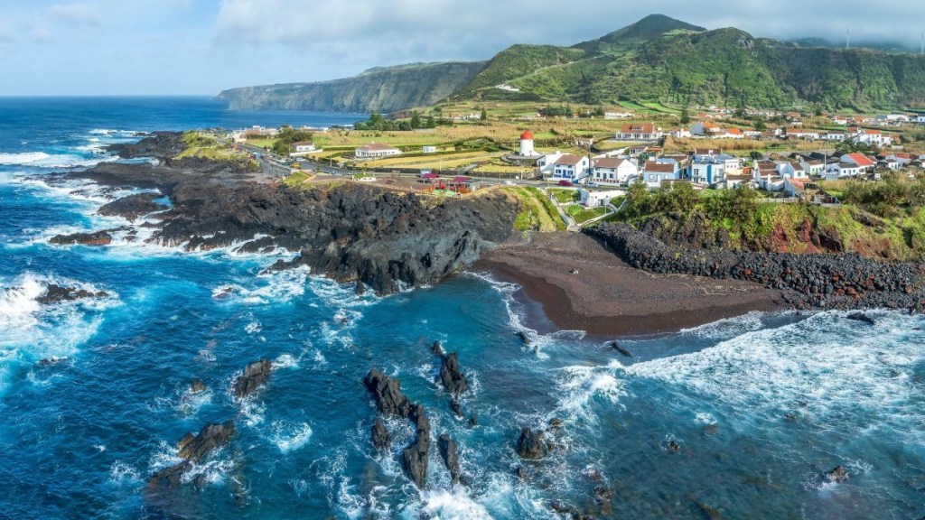 Coastal village with rocky shore, green hills, and a lighthouse.