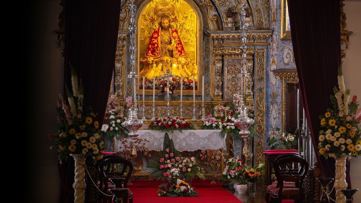 Ornate religious altar with golden statue, candles, and floral arrangements.