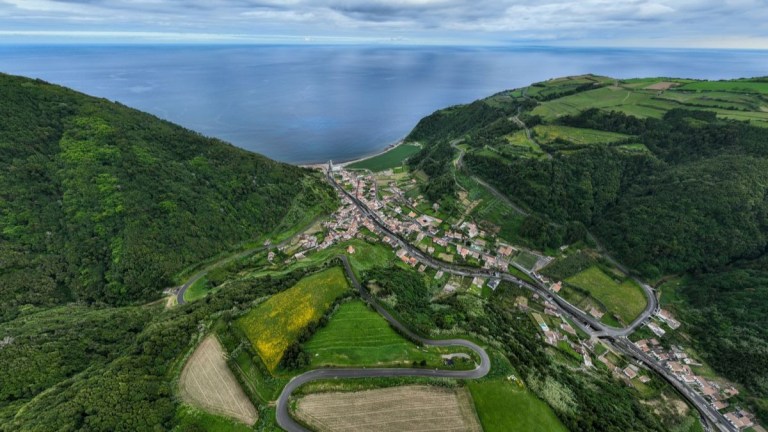 Aerial view of a coastal village with green hills and winding roads.